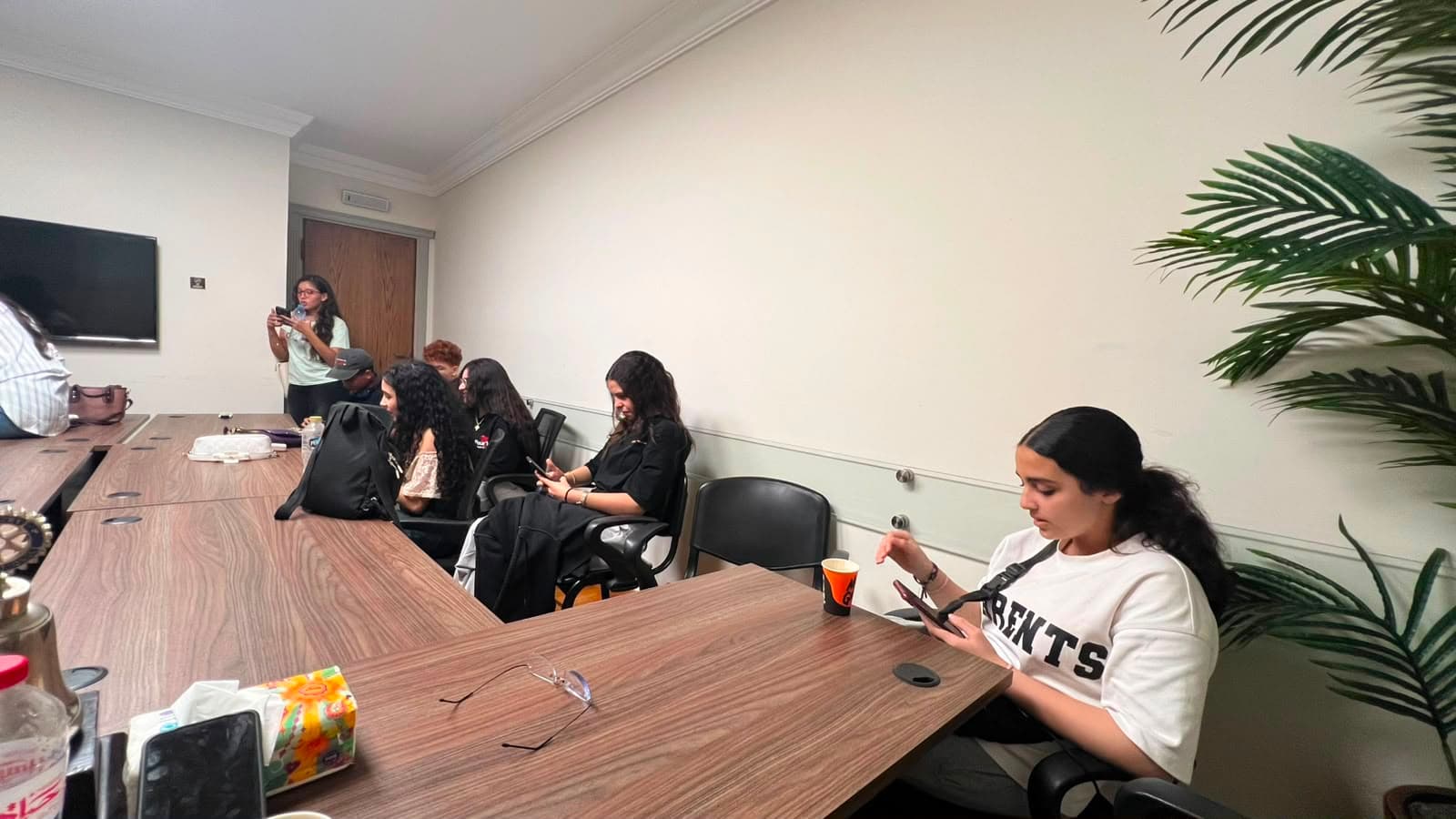 Members around the conference table with phones out during IU video shooting